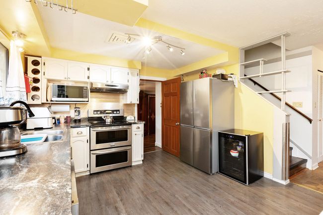 Kitchen featuring appliances with stainless steel finishes, under cabinet range hood, wine cooler, white cabinetry, and wood finished floors | Image 12