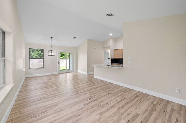 Unfurnished living room featuring light wood finished floors, vaulted ceiling, and a chandelier | Image 4