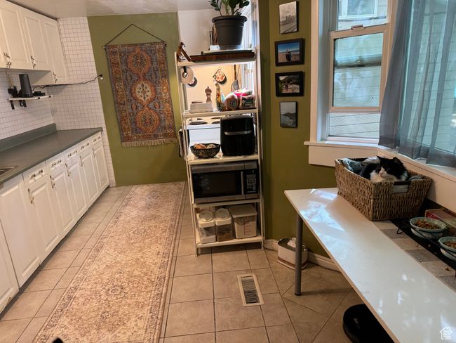 Kitchen with white cabinets, backsplash, dark countertops, light tile patterned floors, and stainless steel microwave | Image 22
