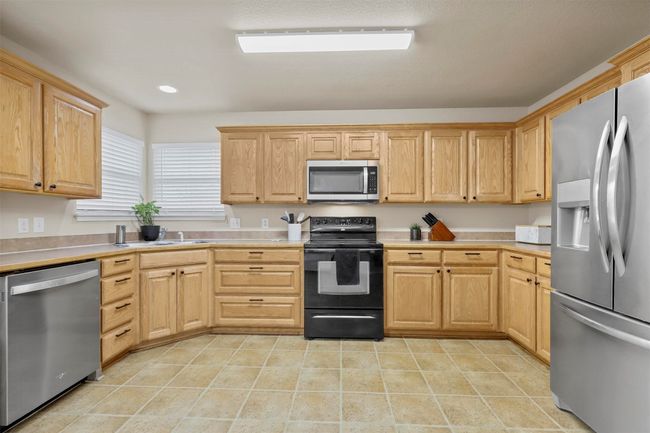Kitchen with light tile patterned floors, stainless steel appliances, light brown cabinets, and light countertops | Image 14