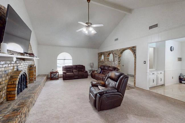Carpeted living room with high vaulted ceiling, a brick fireplace, visible vents, beamed ceiling, and ceiling fan | Image 6