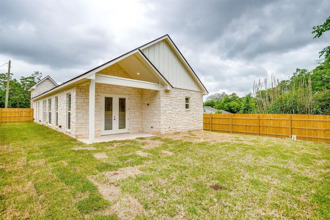 Rear view of property with board and batten siding, french doors, a fenced backyard, a yard, and stone siding | Image 34