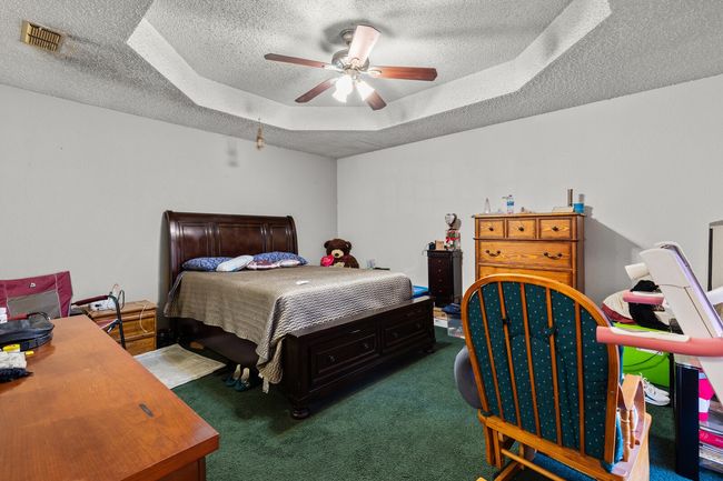Carpeted bedroom featuring ceiling fan, visible vents, a textured ceiling, and a raised ceiling | Image 17