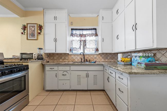 Kitchen with gas stove, ornamental molding, white cabinets, light tile patterned floors, and decorative backsplash | Image 11