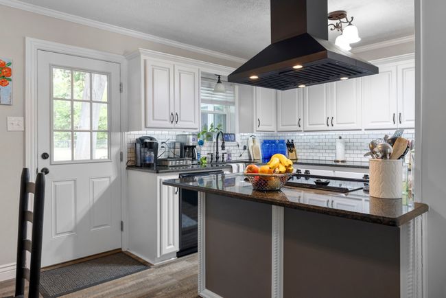 Kitchen with island range hood, ornamental molding, plenty of natural light, wood finished floors, and decorative backsplash | Image 4