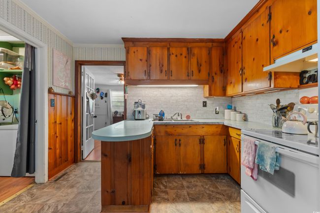 Kitchen featuring white electric stove, under cabinet range hood, stone finish flooring, backsplash, and ornamental molding | Image 17