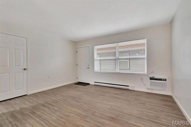 Unfurnished living room featuring a baseboard heating unit, a wall unit AC, and LVP floors | Image 4