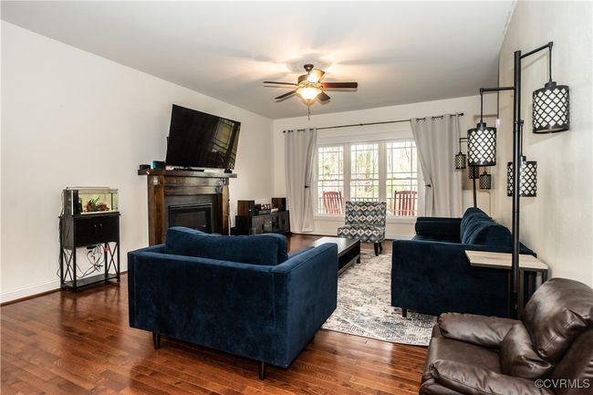 Living room with a ceiling fan, dark wood-style floors, baseboards, and a glass covered fireplace | Image 6