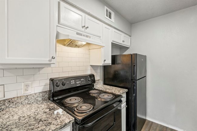 Kitchen featuring black appliances, under cabinet range hood, white cabinets, and dark wood-style flooring | Image 12