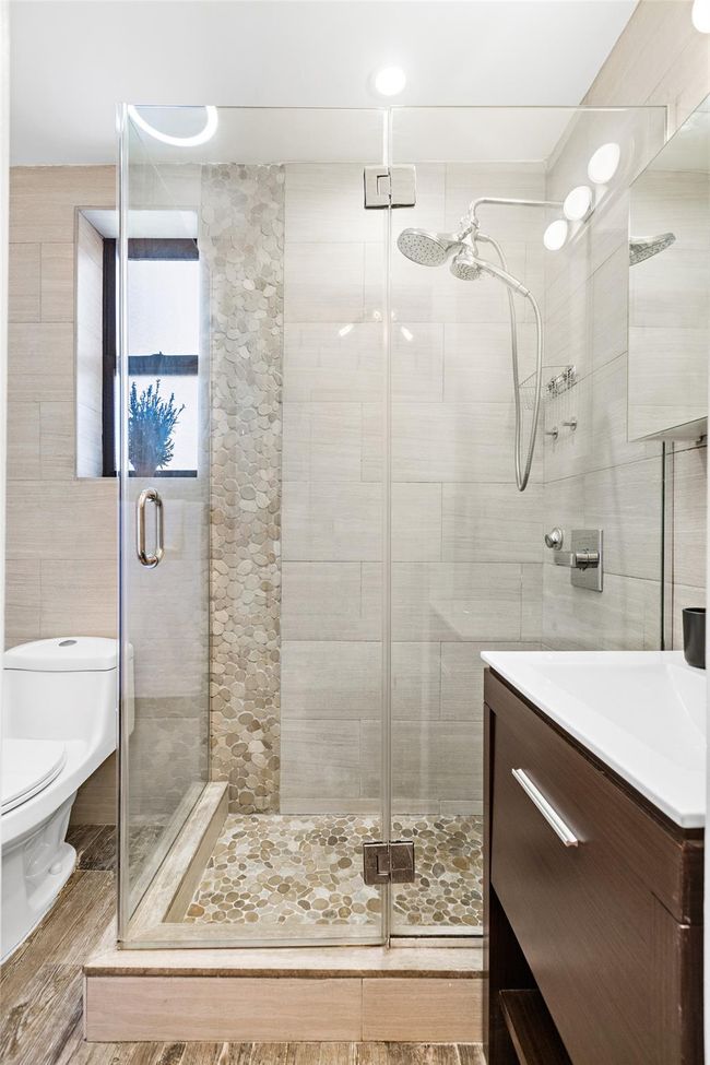 Bathroom featuring tile walls, vanity, toilet, and a stall shower | Image 6
