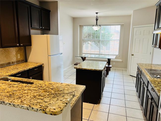 Kitchen featuring light stone counters, hanging light fixtures, a center island, and white refrigerator | Image 9