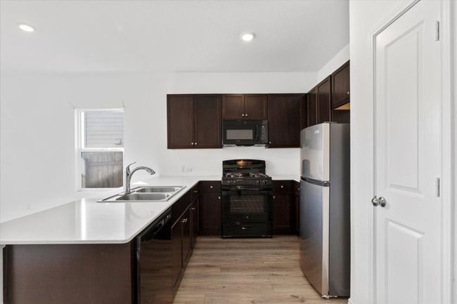 Kitchen featuring black appliances, light wood-style floors, dark brown cabinets, recessed lighting, and light countertops | Image 5