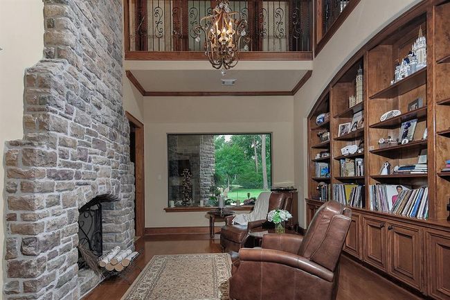 Impressive living room/library/den boasts a stone fireplace, custom built-ins and large, picturesque window. A chandler and upper-level railing add to the sophistication of this space. | Image 9