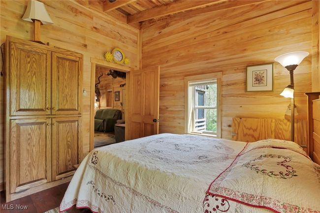 Bedroom with wood walls, dark wood-style flooring, beamed ceiling, and wood ceiling | Image 24