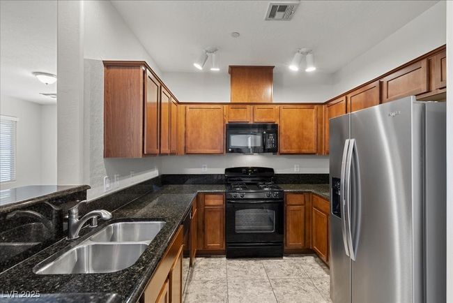 Kitchen with black appliances, brown cabinets, dark stone countertops, and light tile patterned floors | Image 11