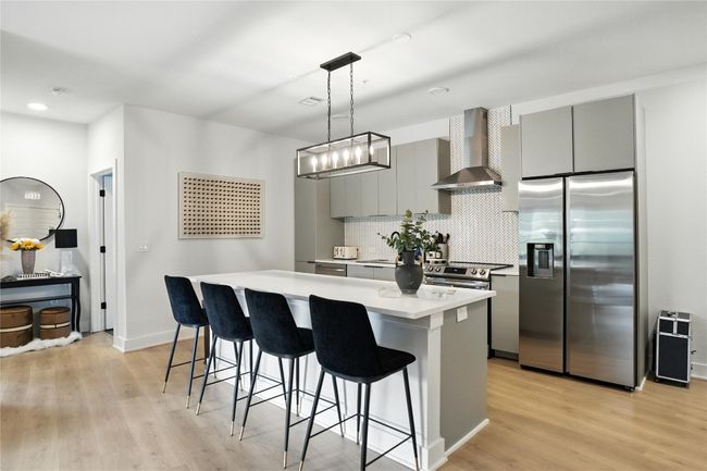 Kitchen featuring stainless steel fridge, wall chimney range hood, gray cabinets, a kitchen breakfast bar, and recessed lighting | Image 5