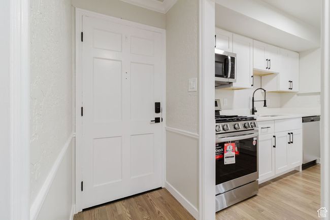 Kitchen featuring light wood finished floors, a sink, stainless steel appliances, white cabinetry, and light countertops | Image 9
