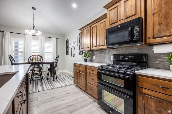 Kitchen with backsplash, light stone countertops, light hardwood / wood-style floors, and black appliances | Image 6