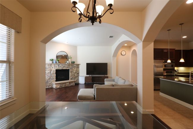 Living area featuring arched walkways, visible vents, a stone fireplace, wood finished floors, and a notable chandelier | Image 8
