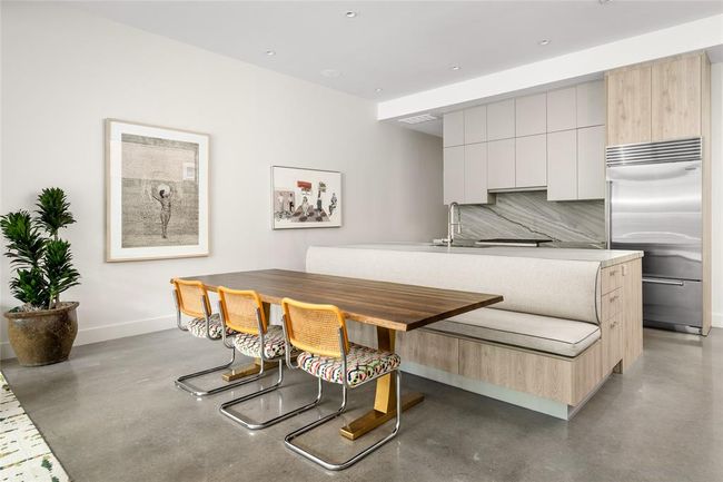 Thoughtfully integrated into the kitchen island, a custom upholstered banquette to create a stylish, space-saving dining area. Sleek cabinetry, dramatic veined Quartzite backsplash, and premium appliances complete the kitchen’s clean, modern aesthetic—offering both beauty and functionality in the heart of the home. | Image 12