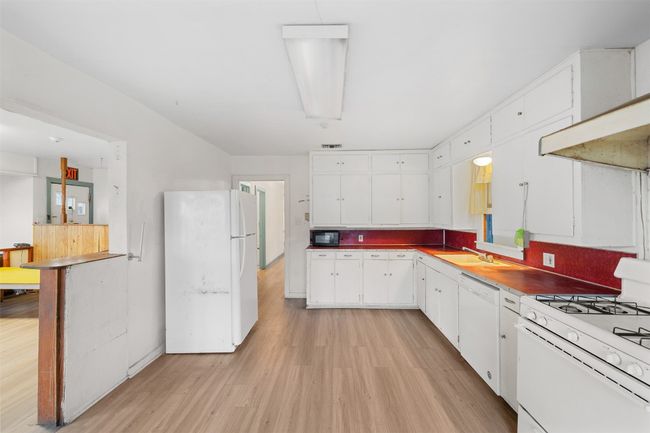 Kitchen with light wood-type flooring, a sink, white appliances, white cabinets, and wall chimney exhaust hood | Image 12