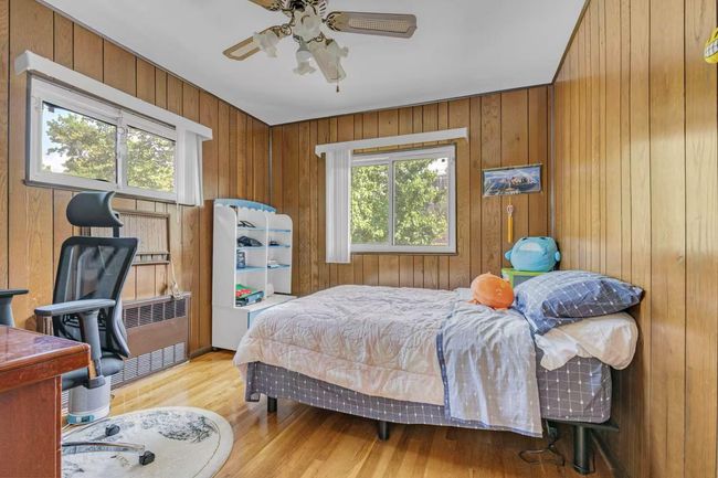 Bedroom featuring multiple windows, light wood finished floors, wooden walls, radiator heating unit, and ceiling fan | Image 10