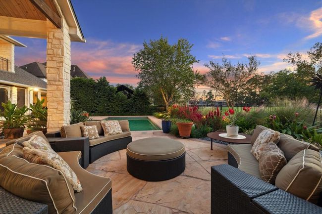 This photo showcases a beautiful outdoor patio, a stone fireplace, and lush landscaping, perfect for relaxing or entertaining. The area overlooks a pool and garden, creating a serene and inviting atmosphere under a stunning sunset sky. | Image 33