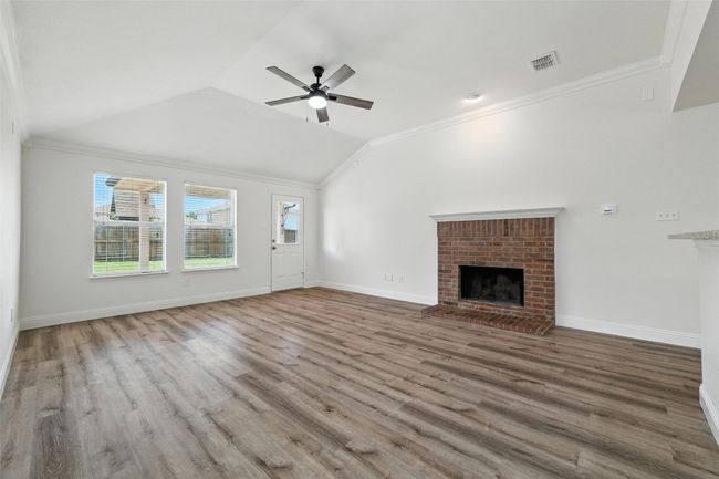 Unfurnished living room featuring a brick fireplace, crown molding, lofted ceiling, wood finished floors, and a ceiling fan | Image 10