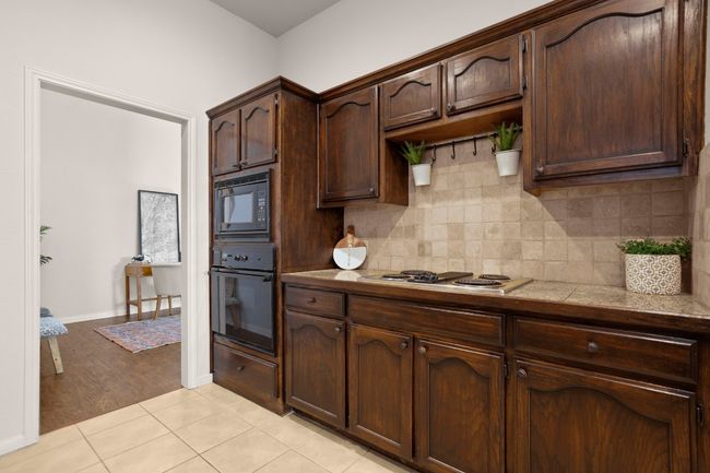 Kitchen with light tile patterned floors, black appliances, decorative backsplash, and dark brown cabinetry | Image 16
