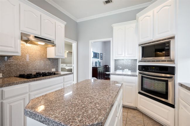 Kitchen with appliances with stainless steel finishes, under cabinet range hood, decorative backsplash, ornamental molding, and white cabinetry | Image 19