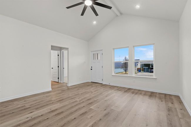 Empty room featuring light wood-type flooring, high vaulted ceiling, beamed ceiling, and ceiling fan | Image 10