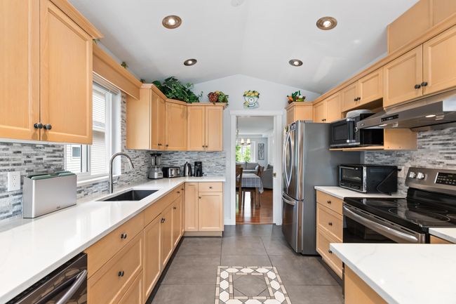 Kitchen featuring a sink, lofted ceiling, under cabinet range hood, light brown cabinetry, and appliances with stainless steel finishes | Image 10