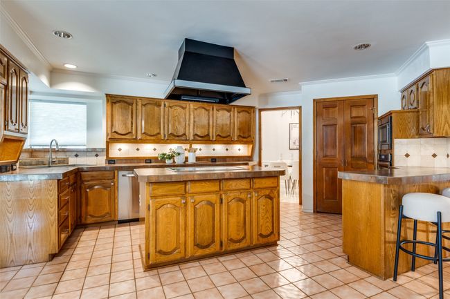 Kitchen with backsplash, ornamental molding, range hood, brown cabinetry, and a breakfast bar | Image 8
