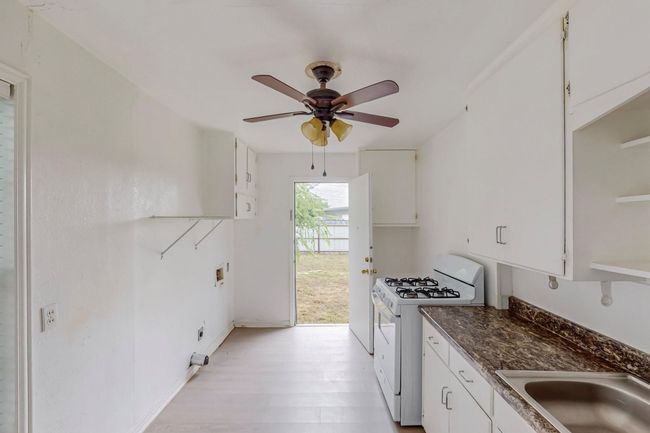 Kitchen featuring white range with gas cooktop, ceiling fan, white cabinetry, dark countertops, and light wood-style floors | Image 8