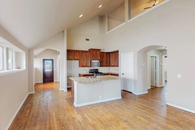 Kitchen featuring stainless steel appliances, arched walkways, light wood finished floors, high vaulted ceiling, and a center island with sink | Image 11