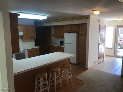 Kitchen featuring white fridge, a kitchen bar, light tile patterned floors, kitchen peninsula, and stainless steel microwave | Image 2