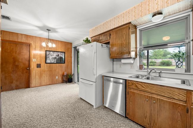 Kitchen with stainless steel dishwasher, brown cabinets, light countertops, freestanding refrigerator, and wood walls | Image 13