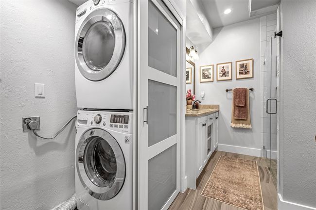 Laundry area featuring stacked washer and clothes dryer, wood finished floors, baseboards, and a textured wall | Image 18