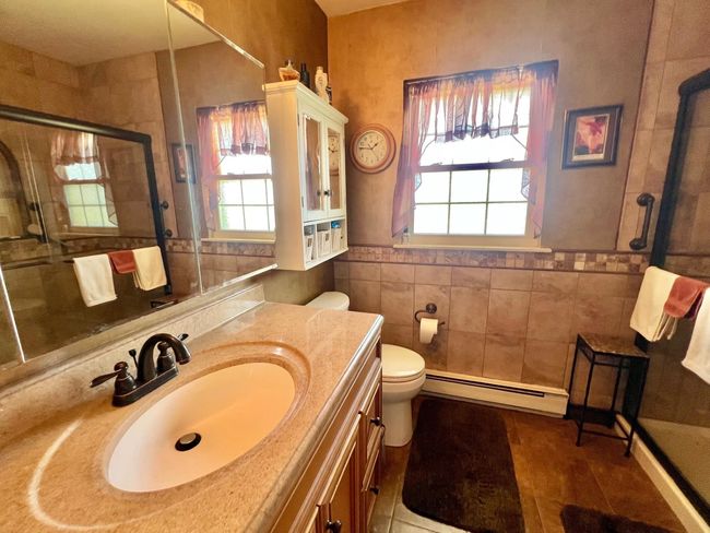 Bathroom featuring a baseboard heating unit, healthy amount of natural light, a stall shower, tile walls, and toilet | Image 14