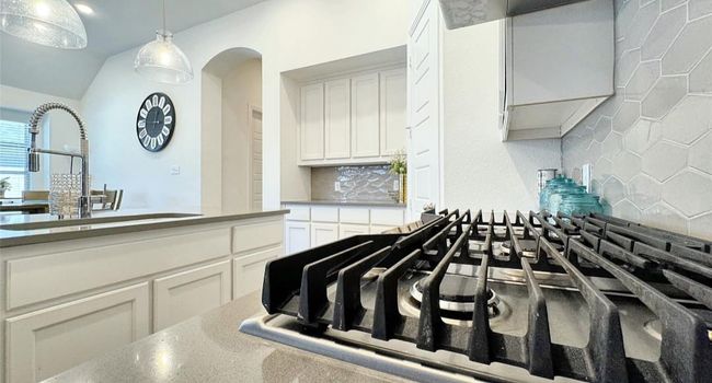 Kitchen with backsplash, a sink, pendant lighting, white cabinetry, and stainless steel gas stovetop | Image 10