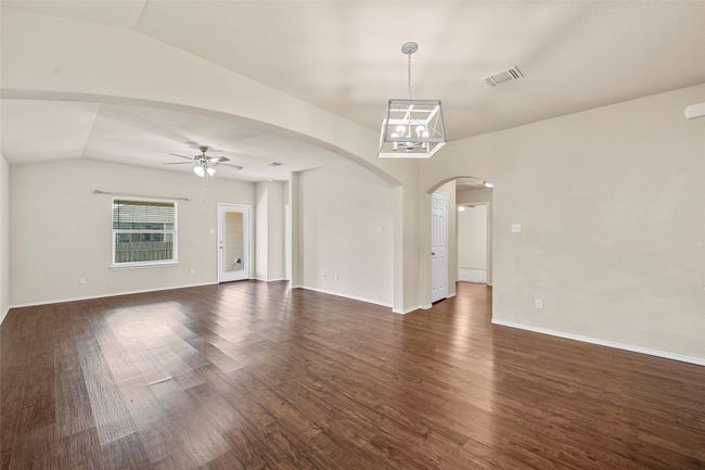 Spare room featuring lofted ceiling, a ceiling fan, arched walkways, dark wood-style floors, and a chandelier | Image 14