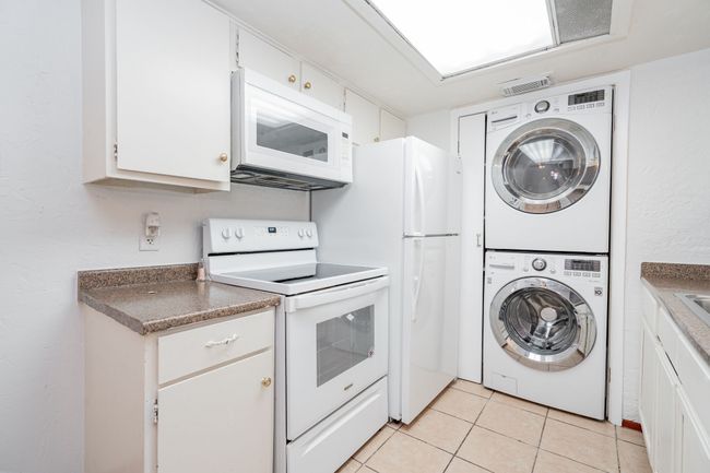 Kitchen with stacked washer / drying machine, visible vents, white appliances, light tile patterned flooring, and white cabinetry | Image 6