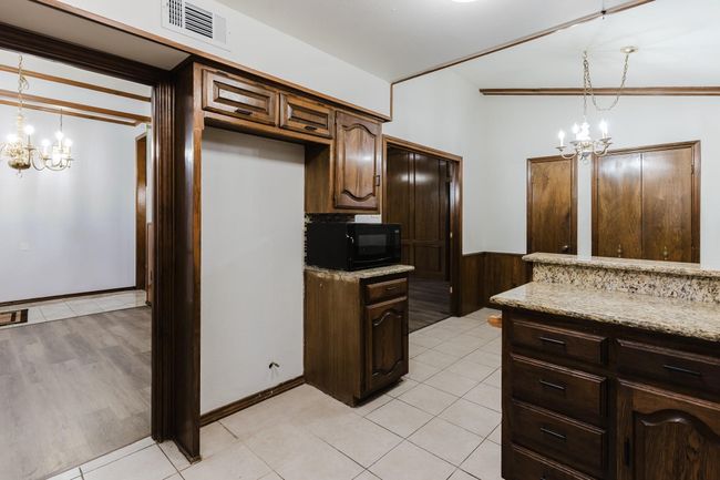 Kitchen featuring visible vents, light stone countertops, black microwave, and a notable chandelier | Image 9
