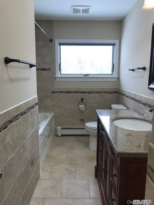 Full bath with a baseboard heating unit, tile walls, vanity | Image 9