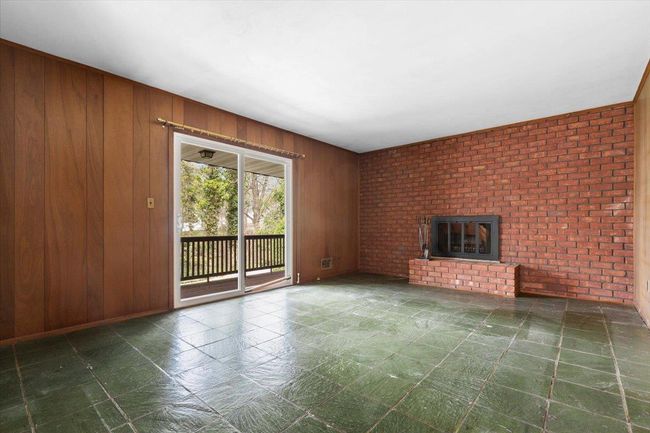 Unfurnished living room featuring brick wall, wood walls, and a fireplace | Image 13