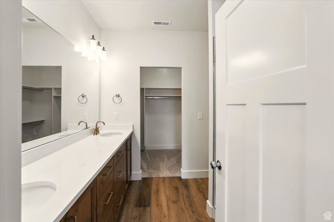 Bathroom featuring wood finished floors, double vanity, a walk in closet, and baseboards | Image 18