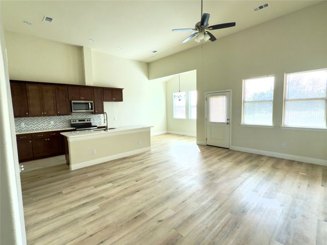 Kitchen with appliances with stainless steel finishes, open floor plan, a ceiling fan, an island with sink, and a high ceiling | Image 37