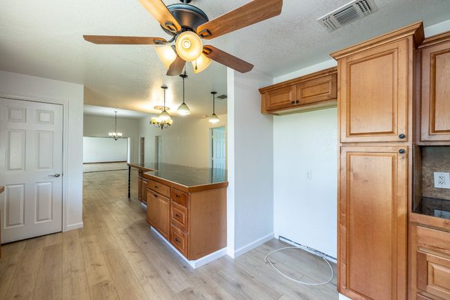 Kitchen featuring light wood-style flooring, brown cabinets, ceiling fan with notable chandelier, and visible vents | Image 12