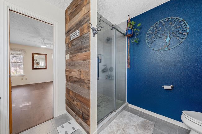 Full bath featuring tile patterned flooring, toilet, a textured ceiling, and a stall shower | Image 19