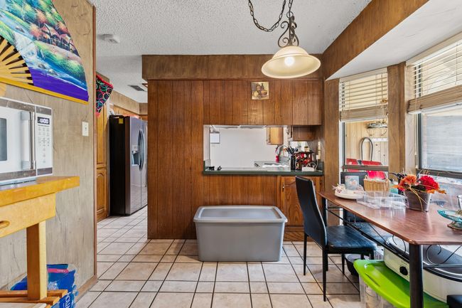 Kitchen featuring a sink, a textured ceiling, brown cabinets, light tile patterned flooring, and stainless steel fridge | Image 24